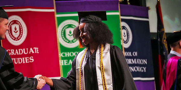 Graduate student shaking hands as she crosses the stage at graduation.